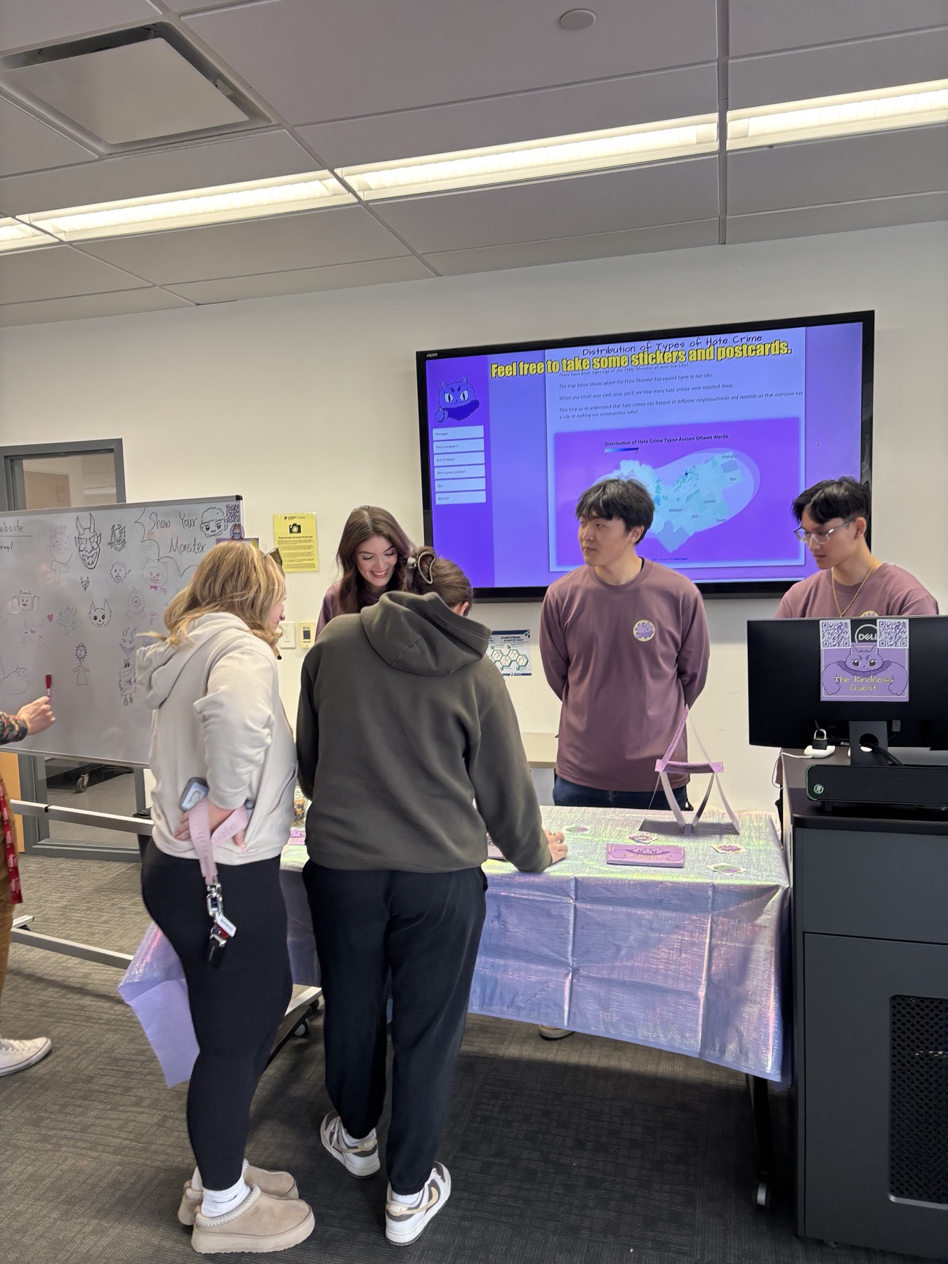 Visitors interacting with The Kindness Quest capstone exhibition while the website is shown on a large screen