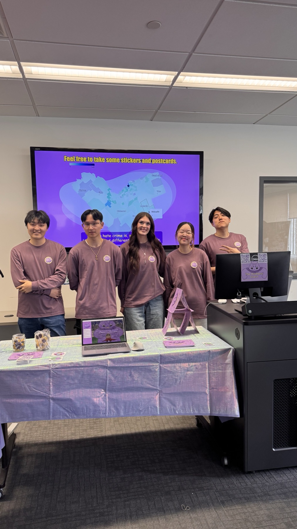 The Kindness Quest team standing at the capstone exhibition booth with laptop demo and display materials